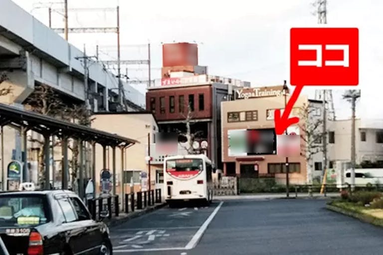 写真は駅に入る階段付近から撮影したもので、バスロータリーの奥にある、オレンジ看板の下が当店入口です。